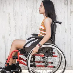 Joven en silla de ruedas, con brazaletes, frente a pared texturizada. La ataxia de Friedreich no detiene su espíritu.