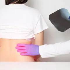 Médico examina radiografía mientras palpa la espalda baja de un paciente, buscando la causa del dolor costillas espalda.