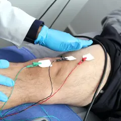 Un profesional médico con guantes azules realiza una electromiografía que es un estudio de la actividad eléctrica de los músculos.
