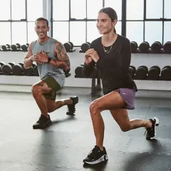 Pareja sonriendo mientras realizan ejercicios aeróbicos en casa, haciendo zancadas.