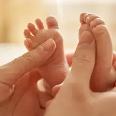 Manos adultas acarician los pies de un bebé, provocando el reflejo de Babinski.