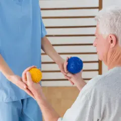 Fisioterapeuta ayuda a un anciano con pelotas de masaje para mejorar la movilidad, un apoyo clave en la lucha contra enfermedades neurodegenerativas.