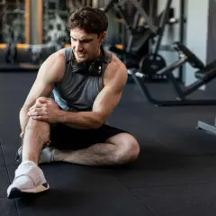 Hombre en el gimnasio con dolor en la rodilla. Aprende cómo prevenir lesiones y entrena seguro.