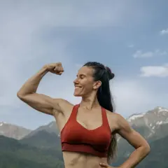 Mujer sonriente muestra su bíceps, demostrando la increíble **función del tejido muscular** en un paisaje montañoso.