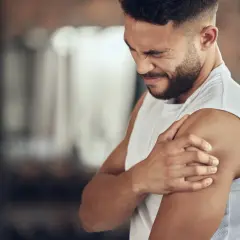 Hombre con expresión de dolor, sujetando su hombro. Podría ser un caso de dolores musculares por ansiedad.