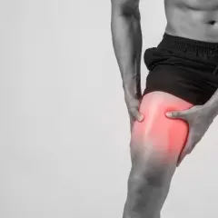 Hombre sujetando su muslo con un área enrojecida, indicando dolor muscular después de entrenar.