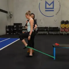 Mujer realizando ejercicios para el dolor de cadera con banda elástica, guiada por un entrenador.