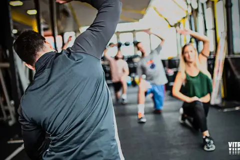 Personas realizando estiramientos dinámicos y estáticos en un gimnasio.