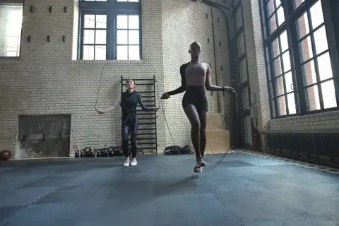Dos mujeres realizan un calentamiento antes de hacer ejercicio, saltando la cuerda en un gimnasio industrial.