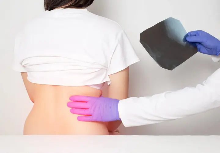 Médico examina radiografía mientras palpa la espalda baja de un paciente, buscando la causa del dolor costillas espalda.
