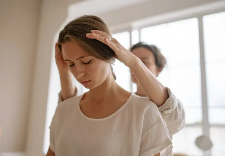 Una persona ayuda a otra a aliviar la tensión en el cuello, sugiriendo un posible alivio para la distonía cervical.