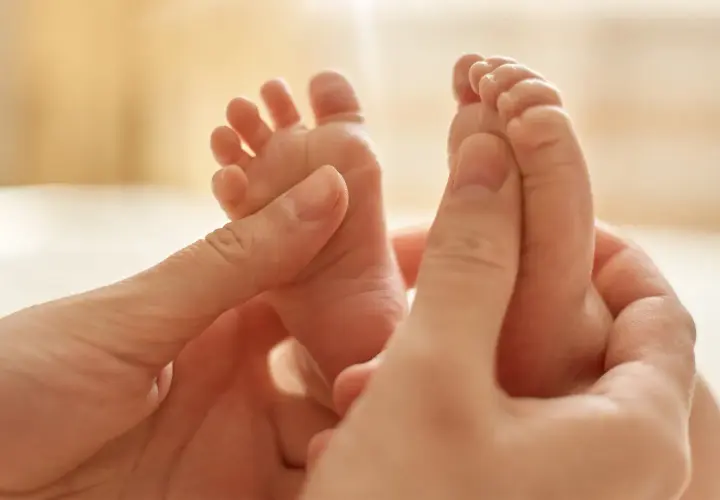 Manos adultas acarician los pies de un bebé, provocando el reflejo de Babinski.