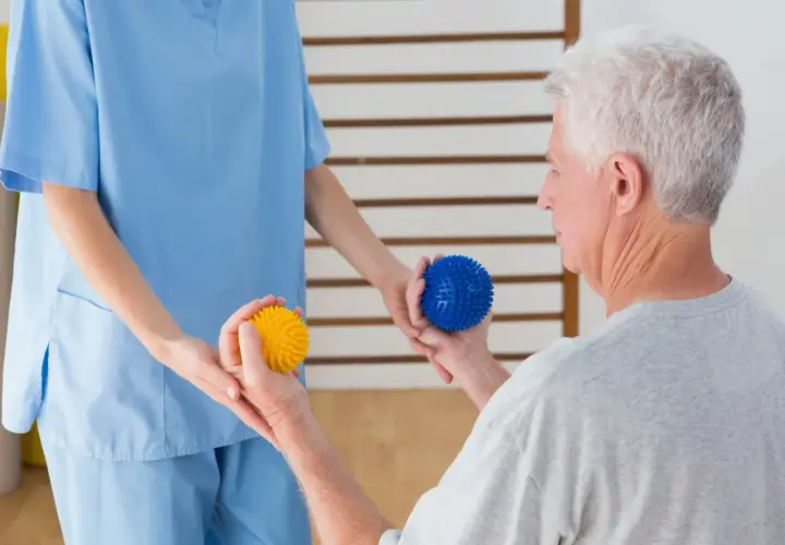 Fisioterapeuta ayuda a un anciano con pelotas de masaje para mejorar la movilidad, un apoyo clave en la lucha contra enfermedades neurodegenerativas.
