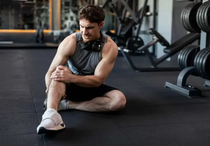 Hombre en el gimnasio con dolor en la rodilla. Aprende cómo prevenir lesiones y entrena seguro.