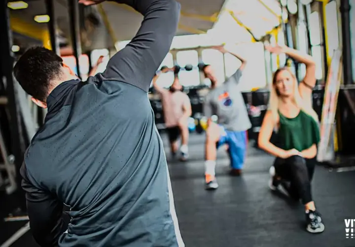 Personas realizando estiramientos dinámicos y estáticos en un gimnasio.