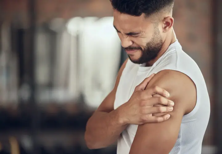 Hombre con expresión de dolor, sujetando su hombro. Podría ser un caso de dolores musculares por ansiedad.