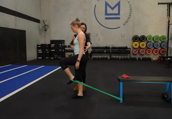 Mujer realizando ejercicios para el dolor de cadera con banda elástica, guiada por un entrenador.