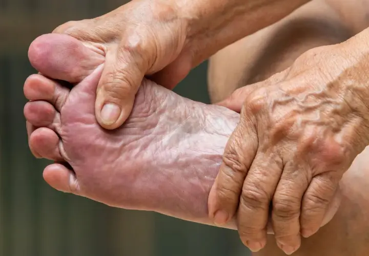 Manos arrugadas masajean un pie, aliviando el dolor de pies.
