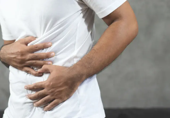 Hombre con las manos en el abdomen, sintiendo una contractura abdominal.