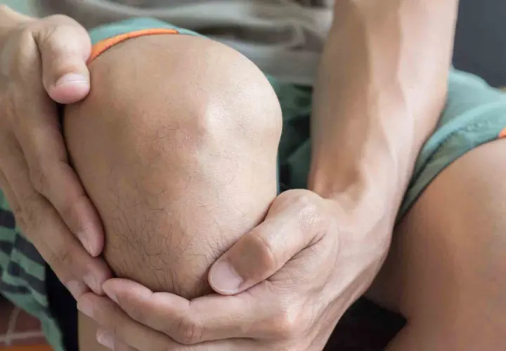Hombre sujetando su rodilla, con expresión de dolor, posiblemente por una rodilla dislocada.