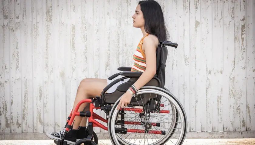 Joven en silla de ruedas, con brazaletes, frente a pared texturizada. La ataxia de Friedreich no detiene su espíritu.