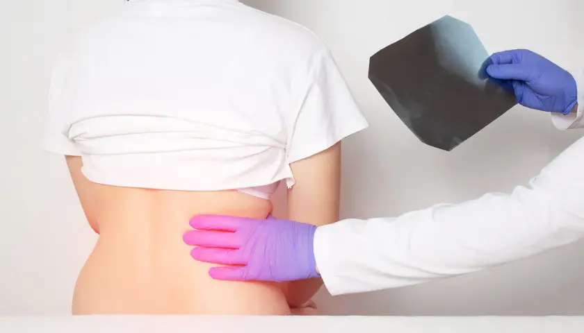 Médico examina radiografía mientras palpa la espalda baja de un paciente, buscando la causa del dolor costillas espalda.