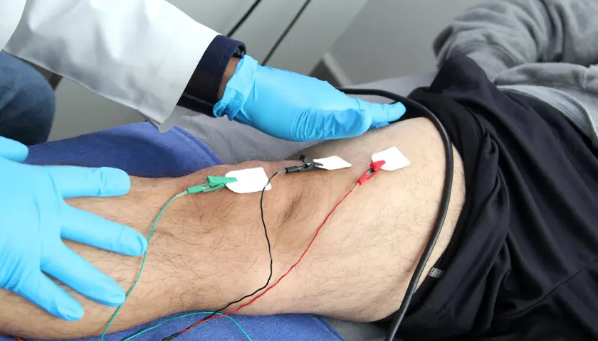 Un profesional médico con guantes azules realiza una electromiografía que es un estudio de la actividad eléctrica de los músculos.