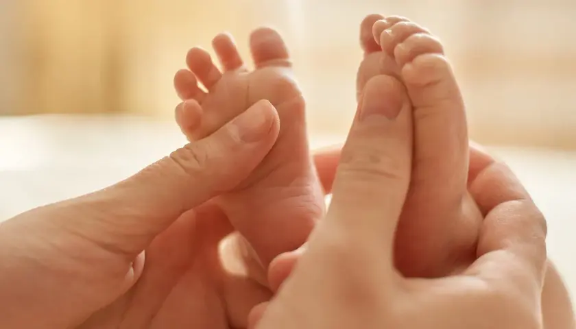 Manos adultas acarician los pies de un bebé, provocando el reflejo de Babinski.