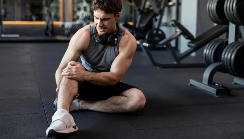 Hombre en el gimnasio con dolor en la rodilla. Aprende cómo prevenir lesiones y entrena seguro.
