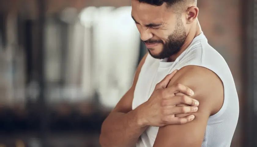 Hombre con expresión de dolor, sujetando su hombro. Podría ser un caso de dolores musculares por ansiedad.