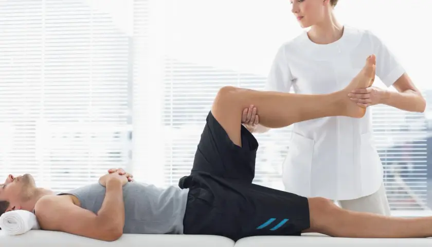 Fisioterapeuta realiza masajes deportivos a un atleta en camilla, enfocándose en la pierna y el pie para aliviar la tensión muscular.