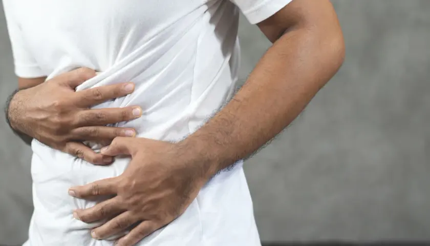 Hombre con las manos en el abdomen, sintiendo una contractura abdominal.