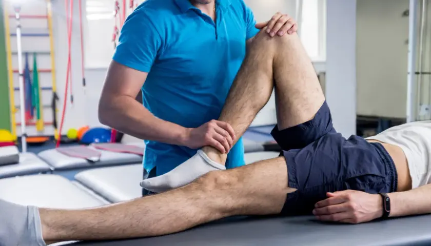 Fisioterapeuta examina la pierna de un paciente, ayudando a aliviar los síntomas de esclerosis múltiple.