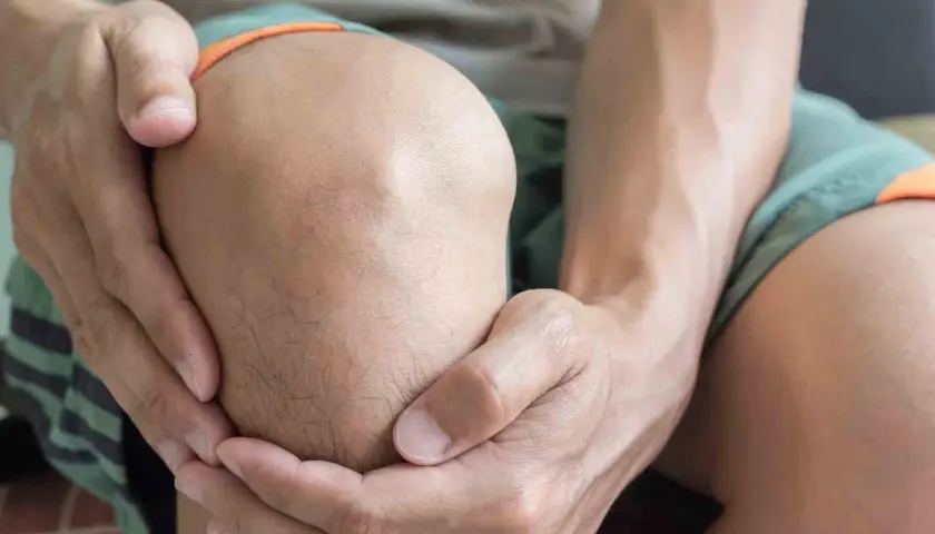 Hombre sujetando su rodilla, con expresión de dolor, posiblemente por una rodilla dislocada.
