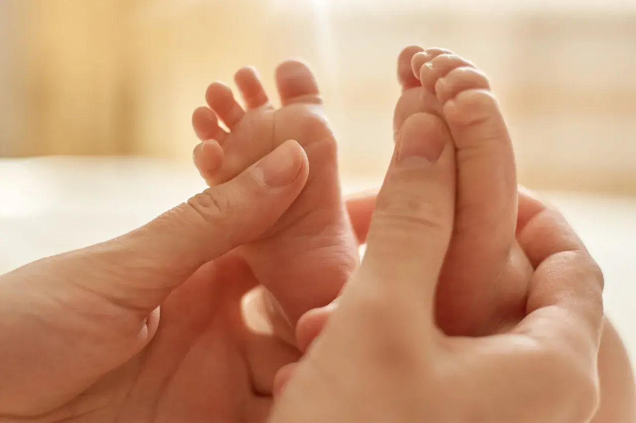 Manos adultas acarician los pies de un bebé, provocando el reflejo de Babinski.