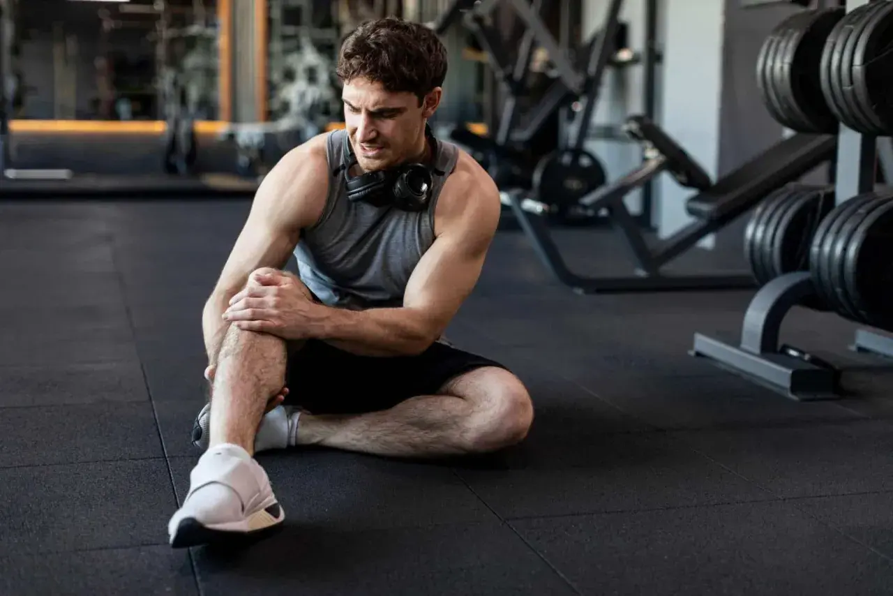 Hombre en el gimnasio con dolor en la rodilla. Aprende cómo prevenir lesiones y entrena seguro.