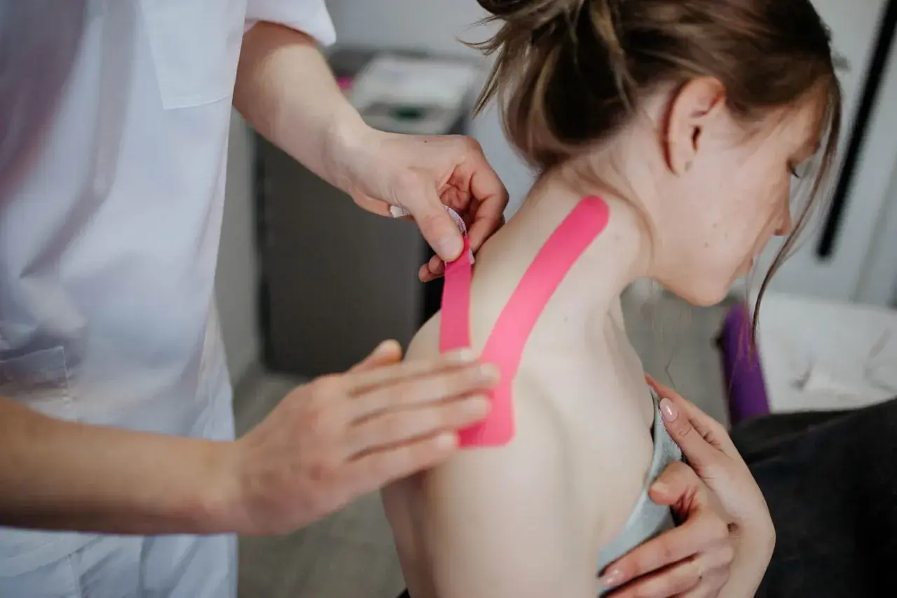 Fisioterapeuta aplica cinta rosa para aliviar dolor de cervicales inflamadas.
