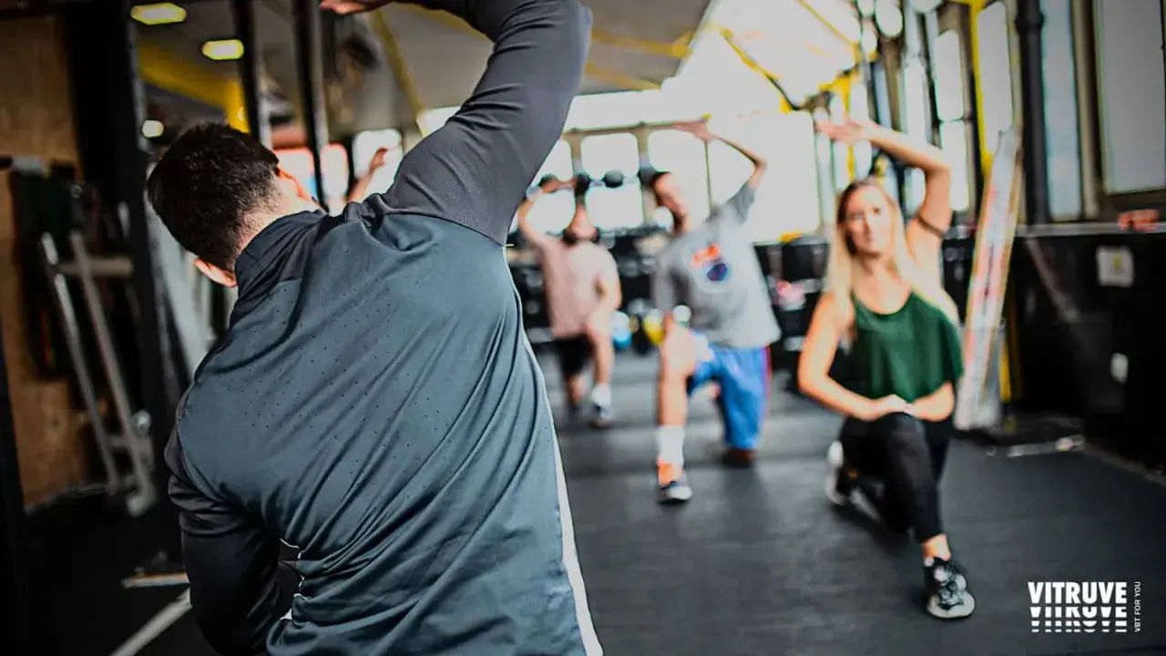 Personas realizando estiramientos dinámicos y estáticos en un gimnasio.