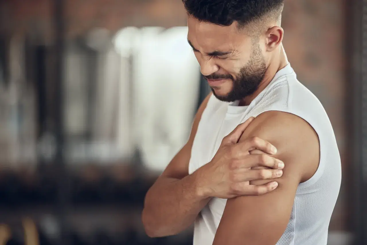 Hombre con expresión de dolor, sujetando su hombro. Podría ser un caso de dolores musculares por ansiedad.
