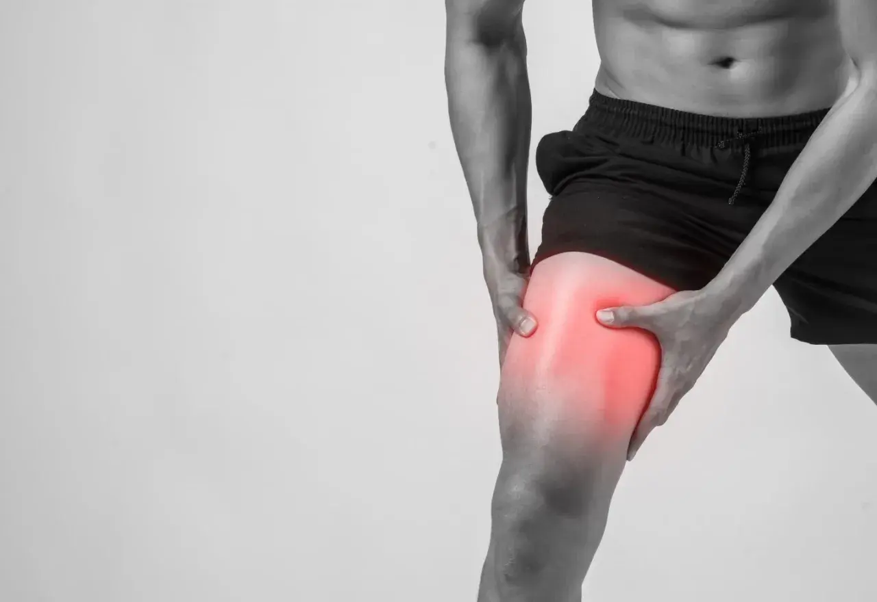 Hombre sujetando su muslo con un área enrojecida, indicando dolor muscular después de entrenar.