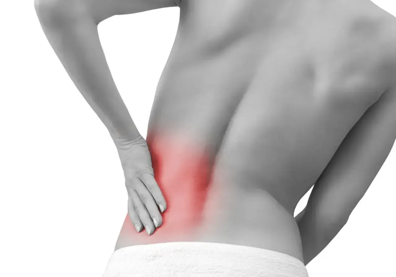 Persona con dolor en la espalda baja, señalando una zona roja que indica contractura lumbar.