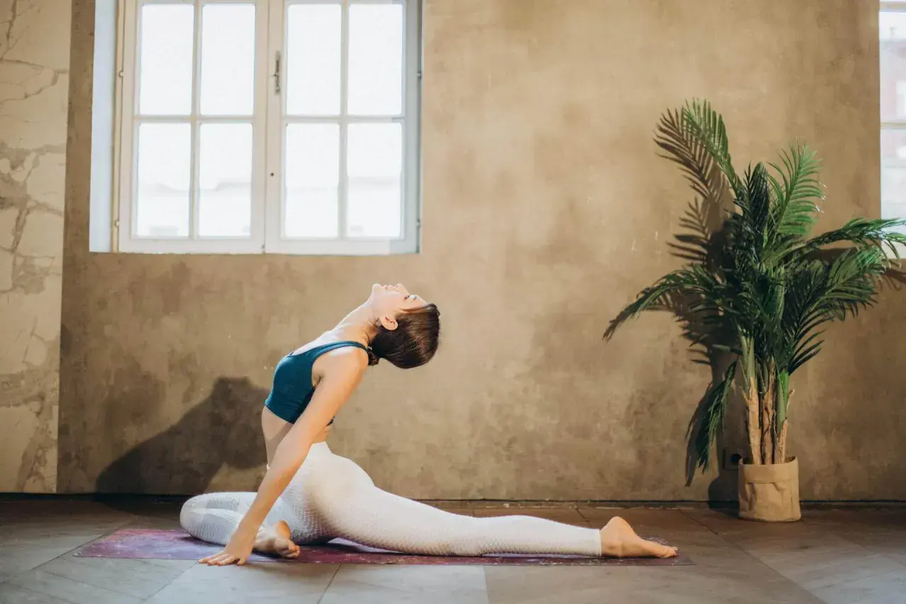 Mujer realiza un profundo estiramiento psoas en una esterilla de yoga, con la espalda arqueada y la cabeza echada hacia atrás.