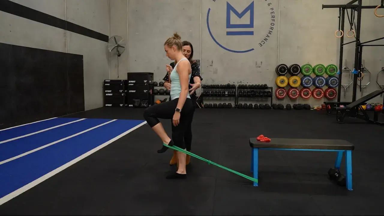 Mujer realizando ejercicios para el dolor de cadera con banda elástica, guiada por un entrenador.