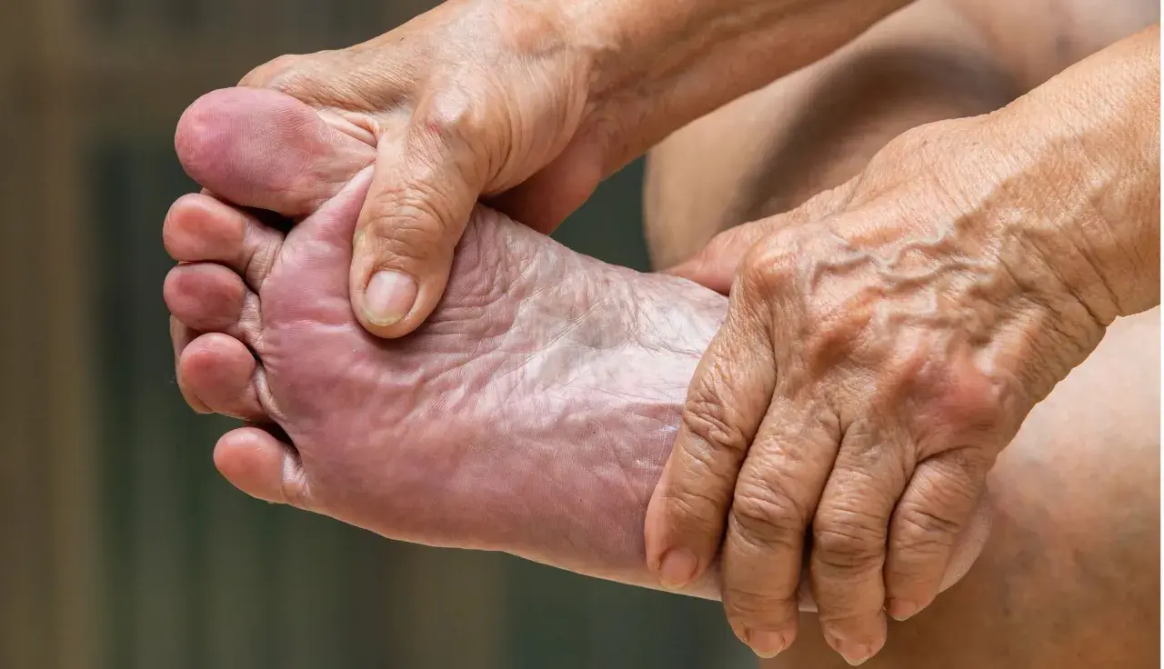 Manos arrugadas masajean un pie, aliviando el dolor de pies.