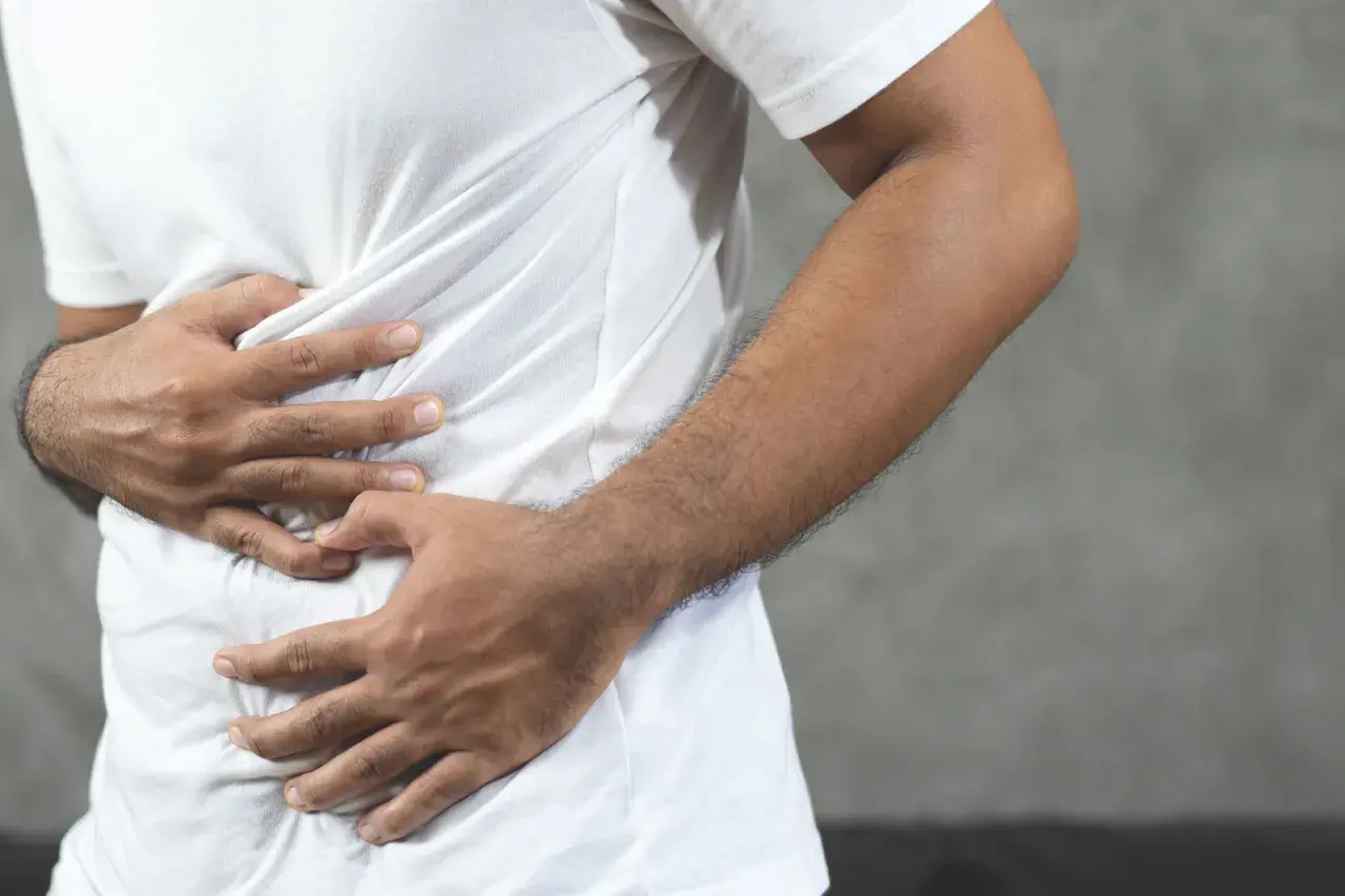 Hombre con las manos en el abdomen, sintiendo una contractura abdominal.