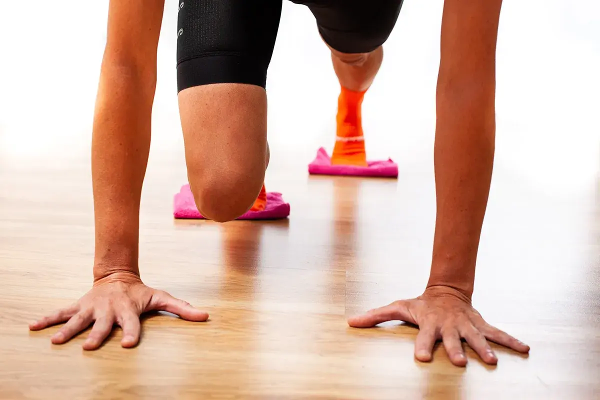 Manos en el suelo, rodillas flexionadas sobre discos deslizantes. Ejercicio para fortalecer rodilla.