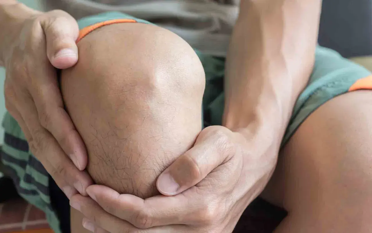 Hombre sujetando su rodilla, con expresión de dolor, posiblemente por una rodilla dislocada.