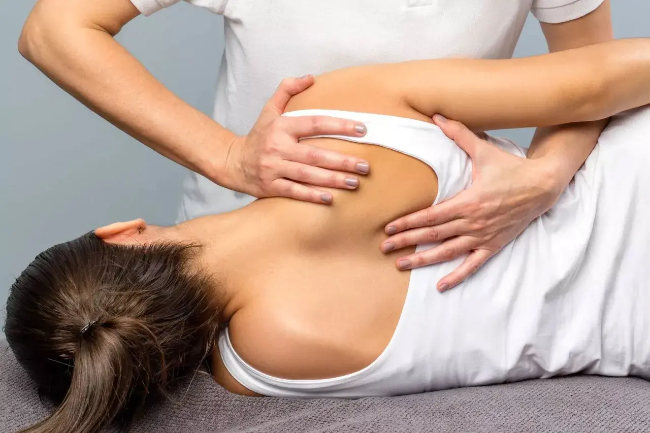 Fisioterapeuta realiza masaje en la espalda de una paciente, ayudando a aliviar el dolor asociado a la fibromialgia.