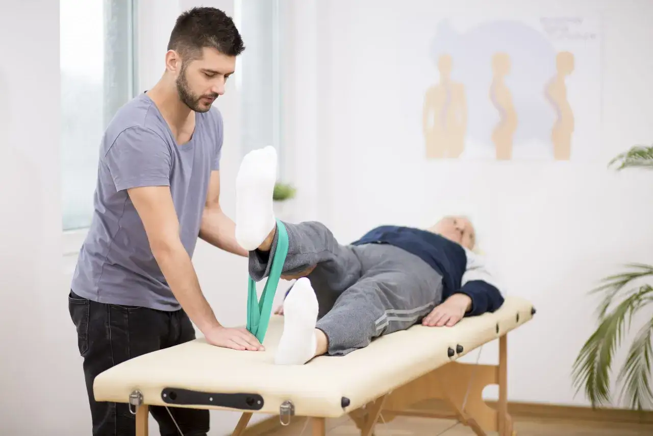 Fisioterapeuta ayuda a paciente a recuperarse de un ictus isqu&eacute;mico con ejercicios de rehabilitaci&oacute;n y banda el&aacute;stica.