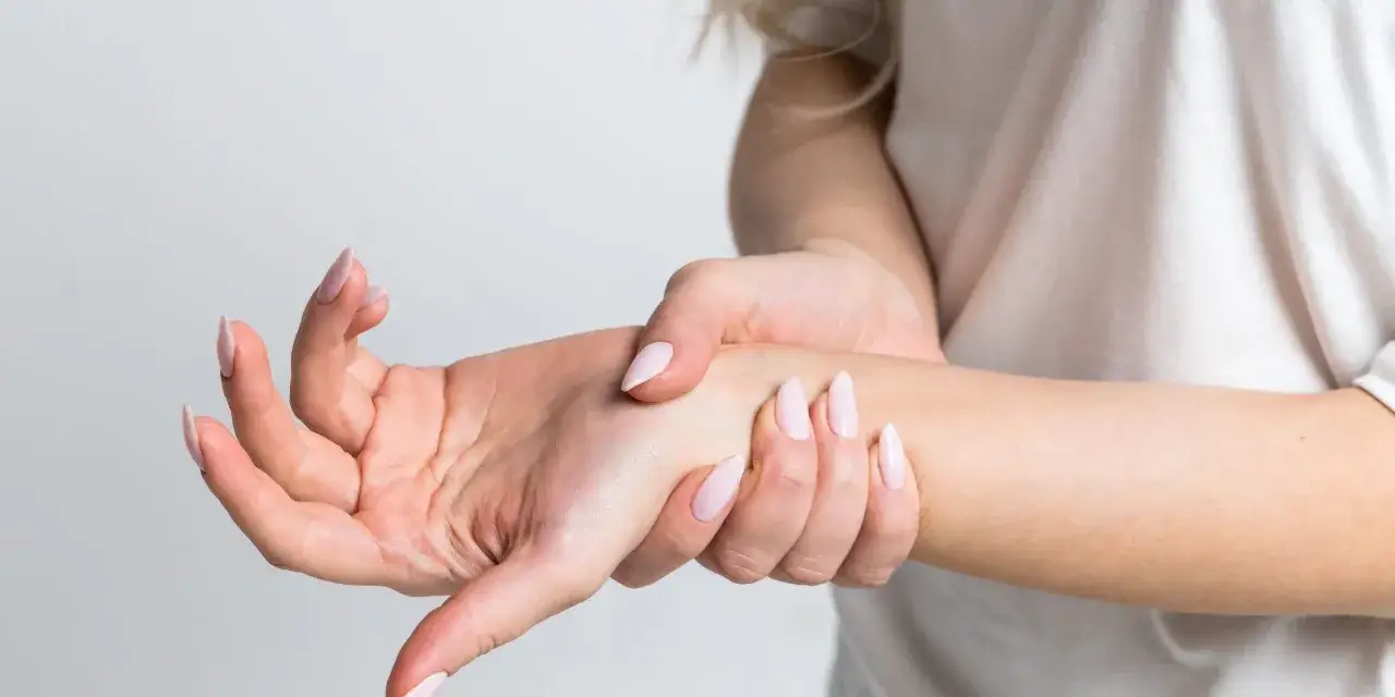 Mano con u&ntilde;as largas sujetando la mu&ntilde;eca, sintiendo el dolor del t&uacute;nel carpiano.
